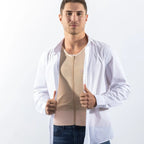 A man modeling a beige zippered compression vest/shaper under an open white button-down shirt, paired with dark blue jeans, against a plain white studio background.