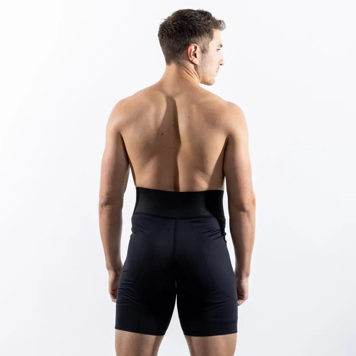 A man viewed from behind wearing black athletic compression shorts against a clean white studio background.