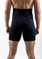 Rear view of a man wearing black athletic compression shorts with a wide waistband, shown against a plain white studio background.
