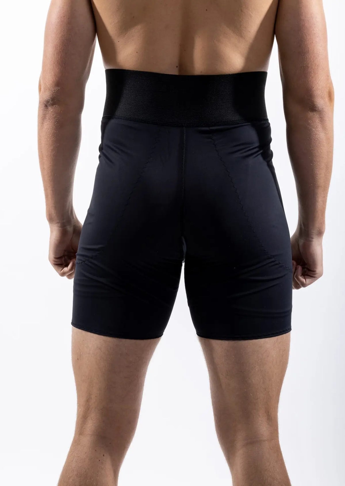 Rear view of a man wearing black athletic compression shorts with a wide waistband, shown against a plain white studio background.