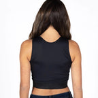 A woman viewed from the back wearing a black sleeveless crop top and dark blue jeans against a plain white background.