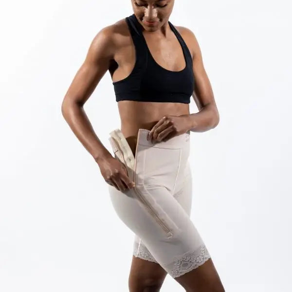 A woman modeling high-waisted white shapewear briefs with lace trim at the hem, paired with a black sports bra, against a solid white studio background.