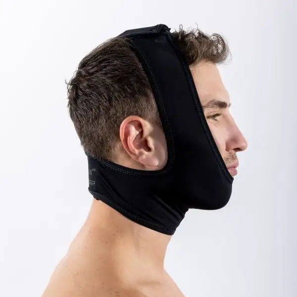 A man shown in side profile wearing a black neoprene head and neck support brace against a plain light gray background.