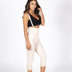 A woman modeling high-waisted, mid-thigh compression or shaping pants in a light cream color, paired with a black crop top, against a plain white studio background.