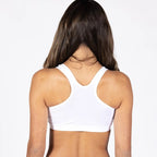 A woman viewed from behind wearing a white racerback crop top and dark blue jeans against a plain white studio background.