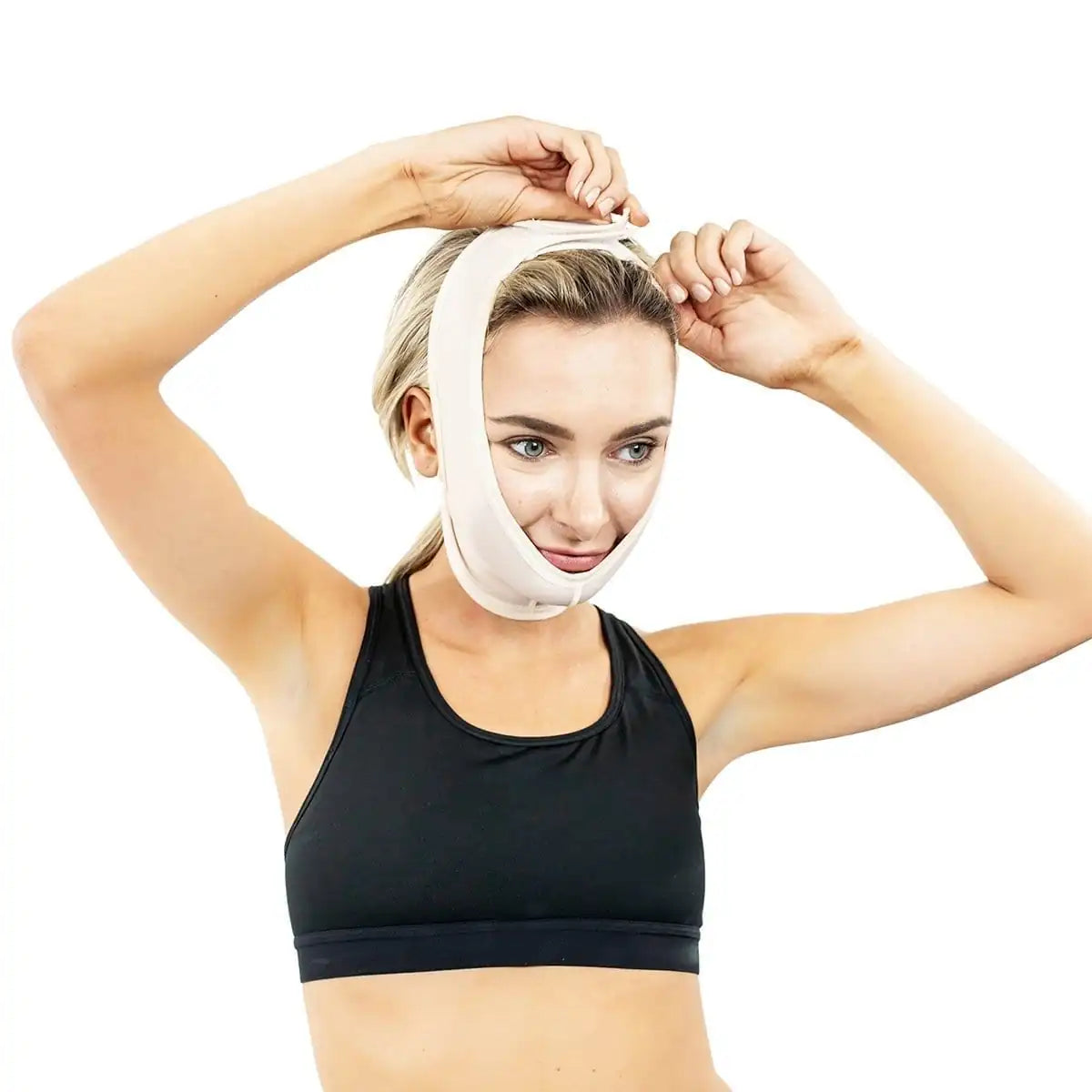 A woman wearing a black sports bra adjusts a white chin and jaw support brace on her head, shown against a plain white background.